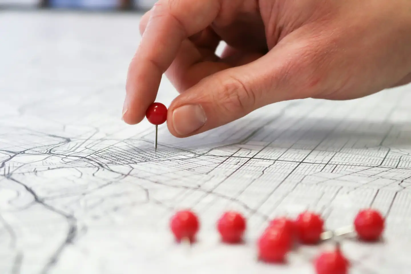Mão cravando um alfinete vermelho num mapa de ruas impresso